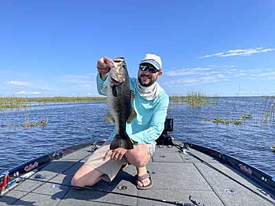 The author with a bass caught on a swim jig around scattered hydrilla near several clumps of reeds.